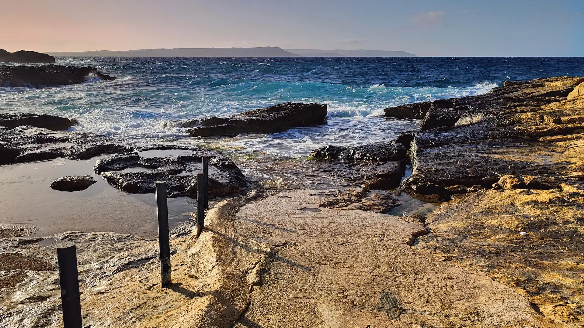 The rocky Gozo shore at ix-Xatt l-Aħmar looking across the channel towards Malta at dusk